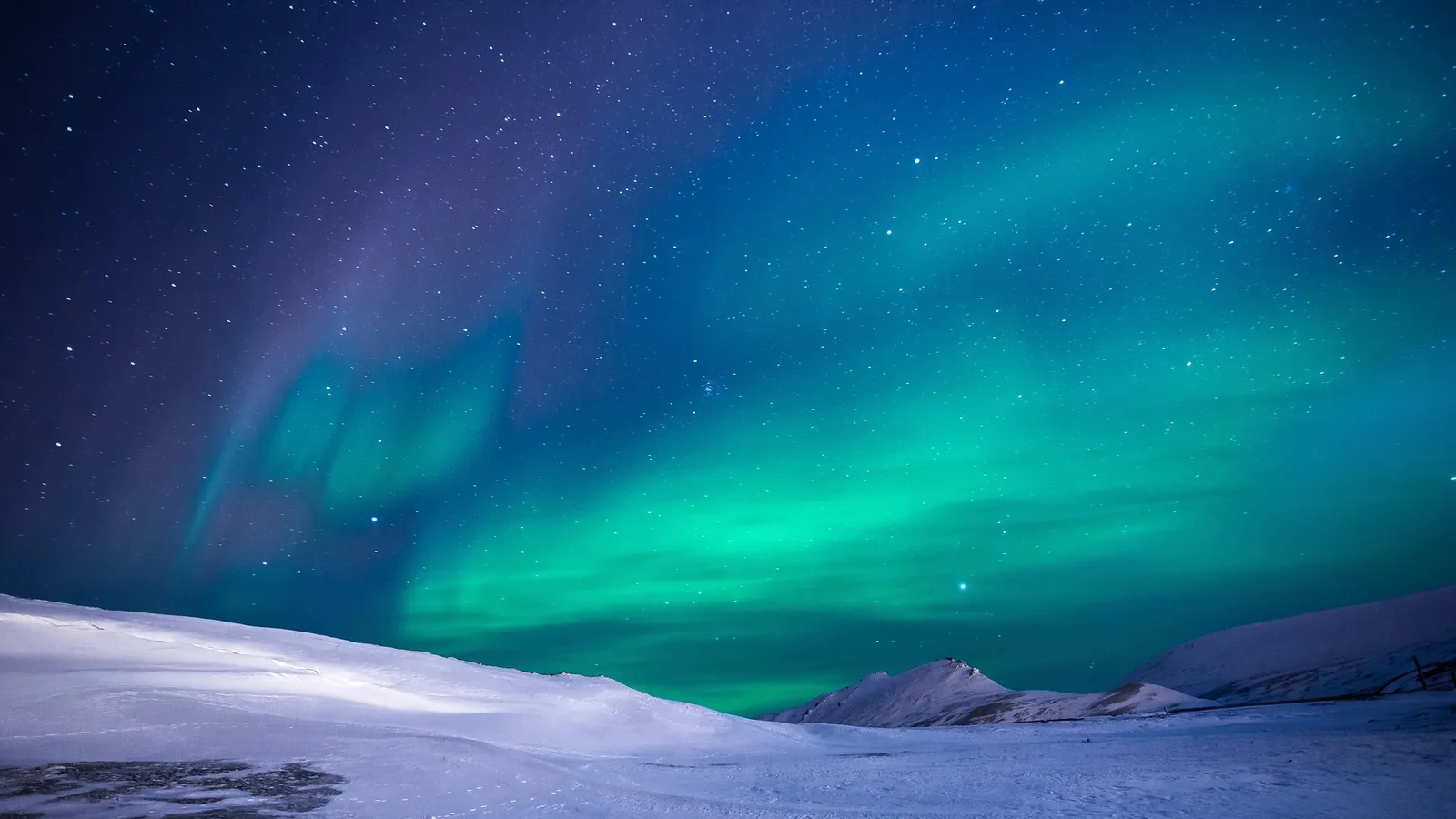 Northern lights glow above a snow-covered landscape. Photo: Noel Bauza / Pixabay